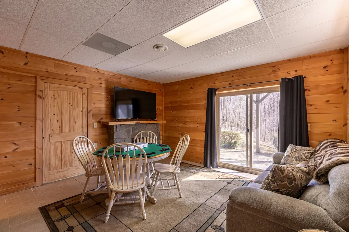 A lively interior scene showcasing a game room with a poker table, comfortable sofa, television, and large window letting in natural light. The setting encourages playful family bonding, game nights, and movie marathons—activities mentioned as part of the home's appeal.