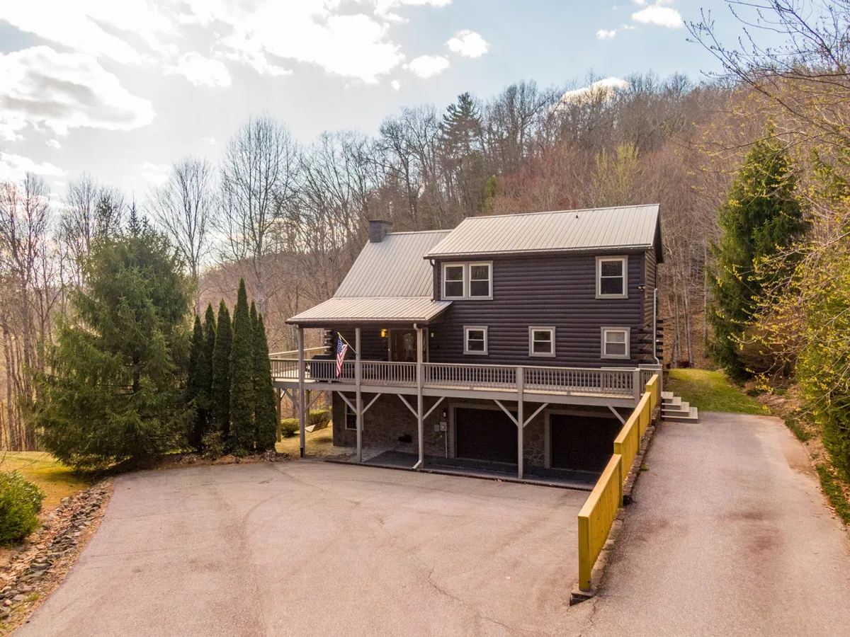 An inviting exterior view of the house, featuring the welcoming porch, surrounded by tall trees and a spacious driveway. The image suggests a relaxed atmosphere, ideal for family gatherings, barbecues, and evenings spent under the stars.