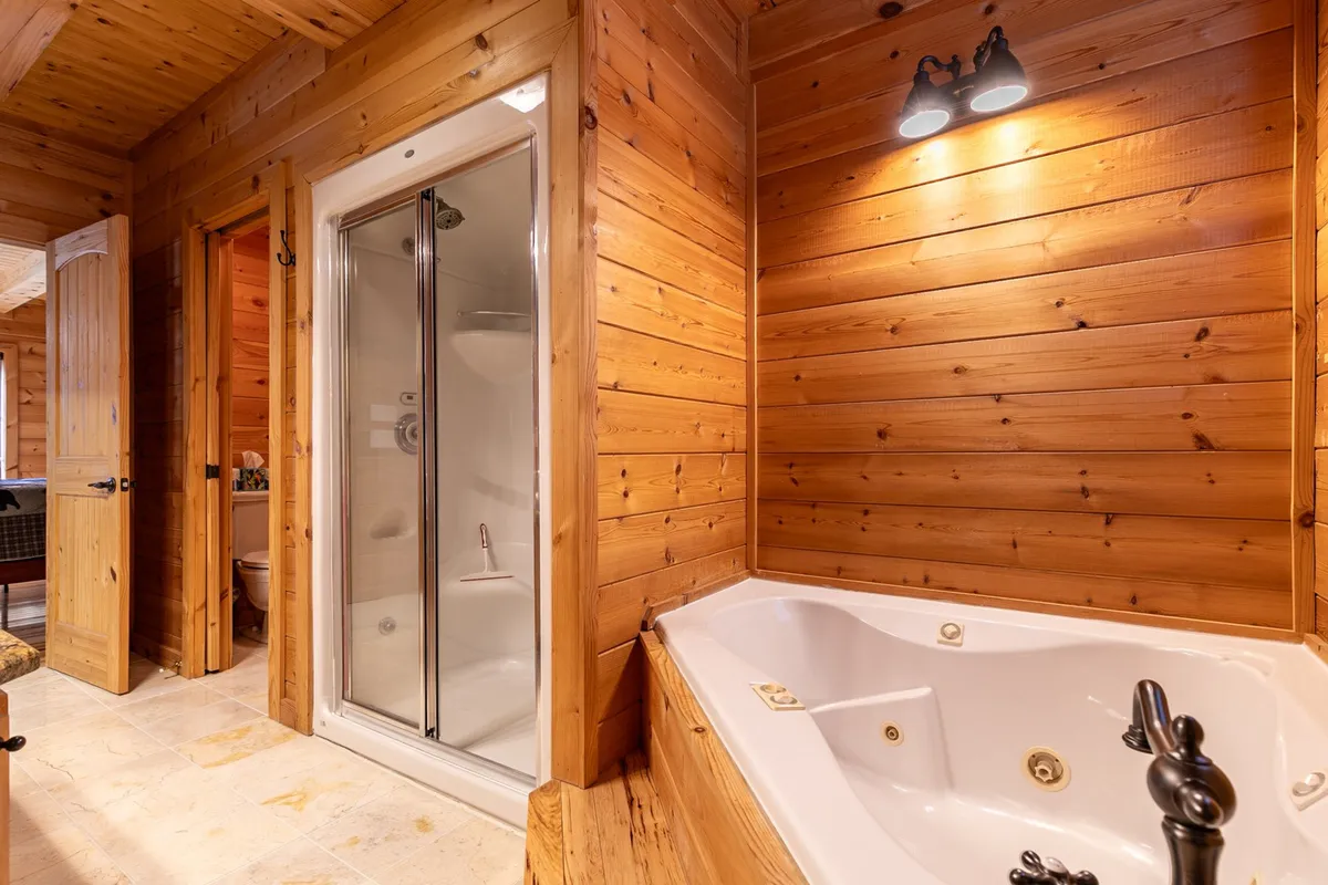 A luxurious bathroom featuring a jacuzzi tub, glass shower, and wooden walls, evoking a spa-like atmosphere. The space is designed for soothing relaxation after outdoor activities, with a calming, tranquil ambiance.
