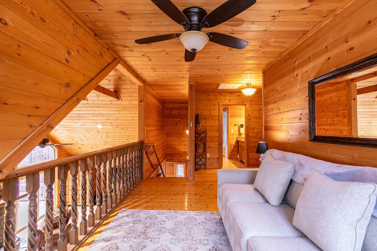 A bright loft space with a comfortable sofa, wooden railing, mirror, and ceiling fan. The setting is inviting and flexible, suitable for lounging, reading, or casual socializing. This could easily represent the loft lounge with a pull-out sleeper sofa, ideal for sleepovers or late-night chats as described in the content.