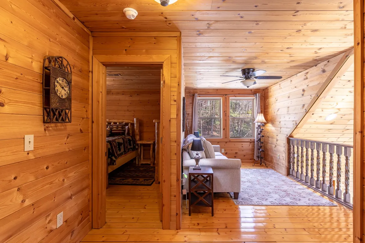 A cozy living area with wooden walls and a comfortable sofa set beside large windows, allowing natural light to stream in. The windows open up to tranquil nature views, inviting the outside in and providing a seamless connection to the outdoors.