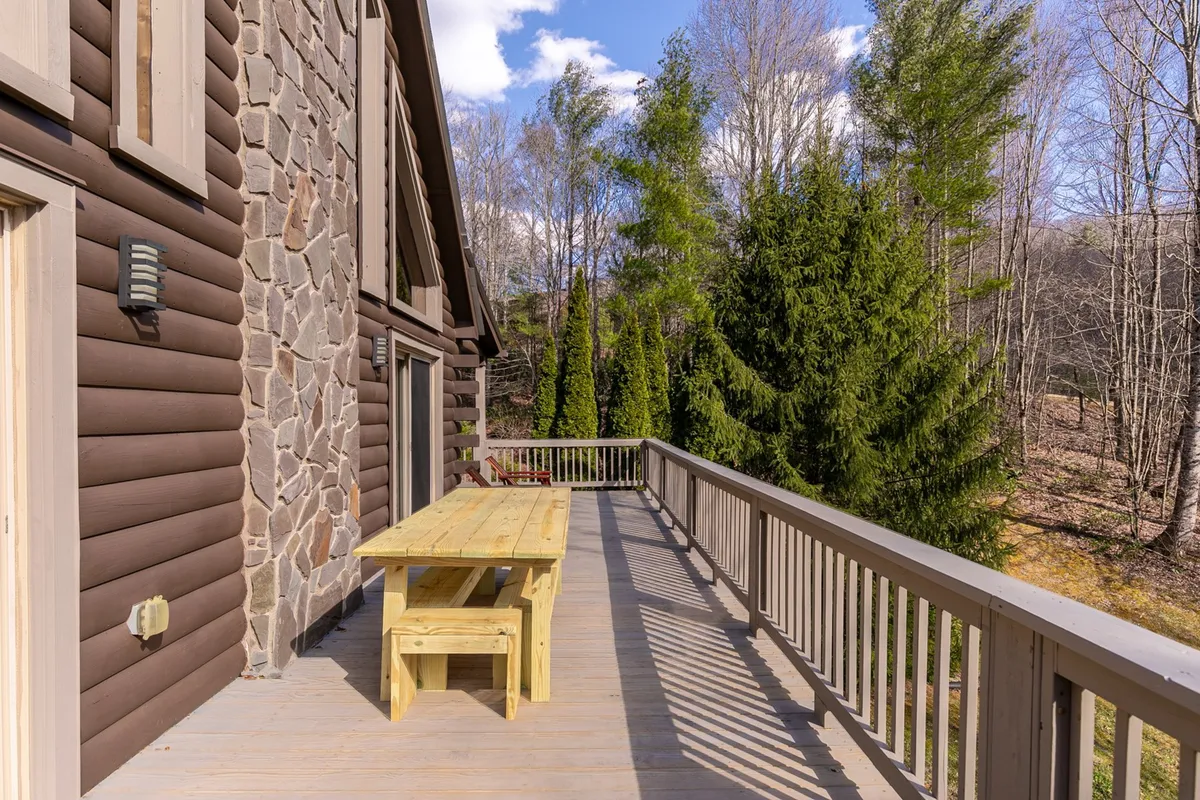This image captures a wooden picnic table set on a spacious deck, bordered by a rustic stone wall and surrounded by lush green trees. The outdoor space invites group gatherings and al fresco dining, with ample room for everyone to relax and enjoy the scenery.